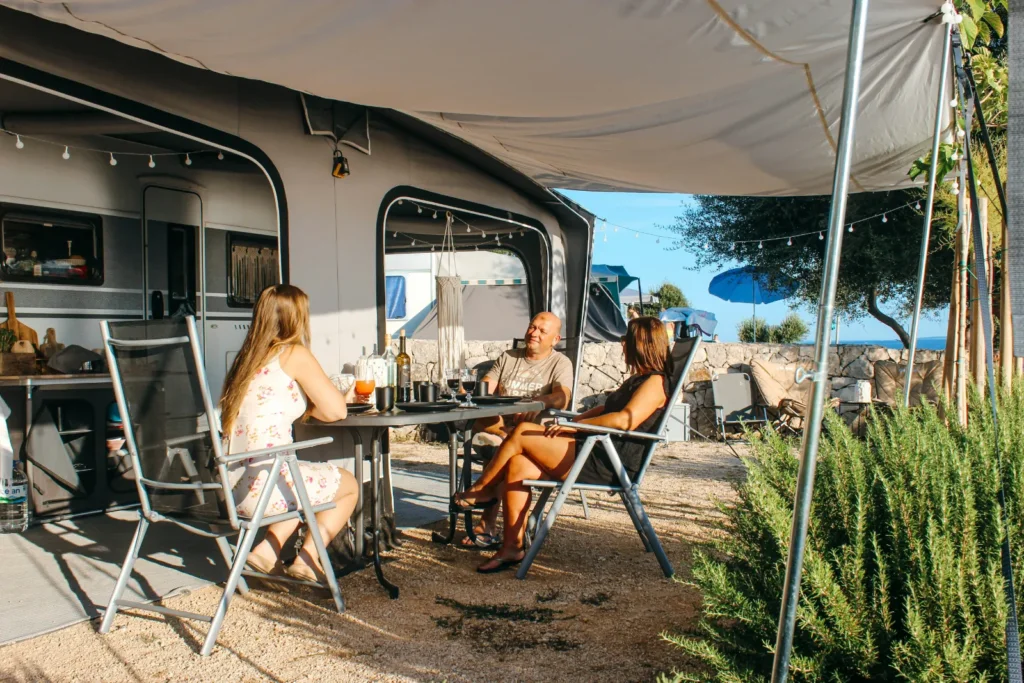 Caravan with awning set up next to the beach with people sitting underneath it, enjoying the shade